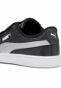 Schwarze und silberne Turnschuhe mit einer strukturierten Oberseite, ausgestattet mit einem Riemenverschluss, weißen Sohlen und Puma-Logo an der Ferse und der Seite.