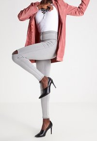 Light pink zip-up jacket, white ribbed bodysuit, distressed grey skinny jeans, and black high-heeled shoes in a dynamic pose.