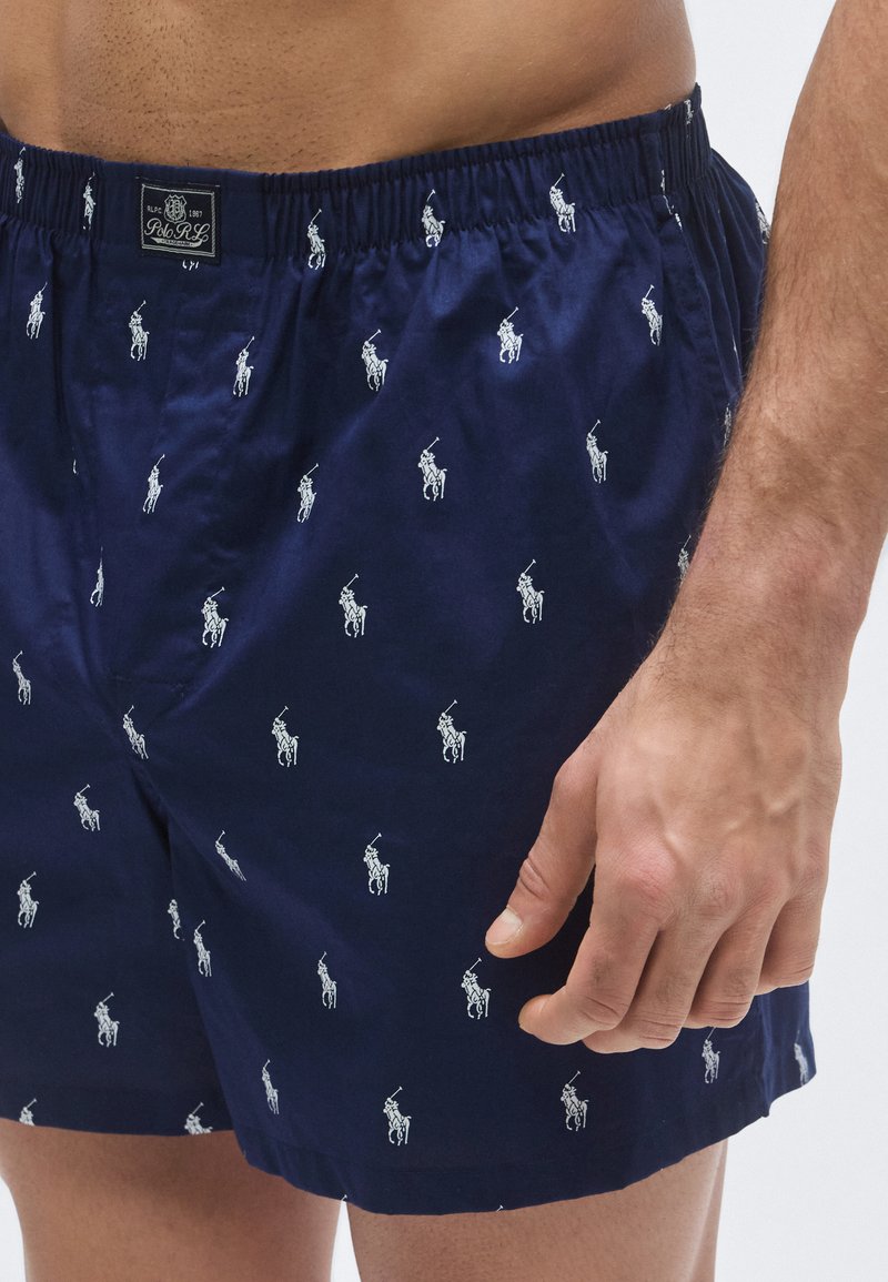 Navy blue boxer shorts made of cotton, featuring a repetitive white polo player logo pattern. Elastic waistband for comfort.