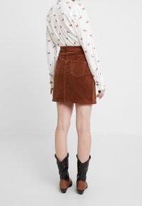 Minigonna marrone in velluto a coste con vita alta, due tasche posteriori e una texture liscia, abbinata a una camicia stampata a maniche lunghe e stivali da cowboy.