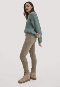 Lichtblauwe gebreide trui, beige corduroy broek en tan enkelbotten. De trui heeft een relaxte pasvorm, terwijl de broek zijzakken heeft.