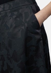 Schwarzer Rock mit floralen Mustern und glatter Textur, ausgestattet mit einer seitlichen Tasche und einem subtilen Glanz, der die komplizierten Designmerkmale betont.