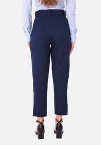 Pantaloni blu navy su misura con vita media, tessuto morbido e lunghezza cropped. Abbinati a scarpe nere con tacco a blocco.