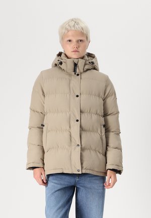 Veste doudoune beige avec une capuche, texture matelassée, boutons à pression sur le devant et poches latérales. Portée par-dessus un jean bleu clair.