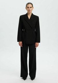 Blazer noir ajusté avec un design enveloppant, des manches longues et une ceinture amovible. Associe à un pantalon noir à jambes larges et des chaussures noires à bouts pointus.
