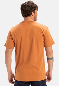 Short-sleeve orange cotton t-shirt with a crew neck, relaxed fit, and a smooth texture. Visible stitching and a subtle curve at the hem.