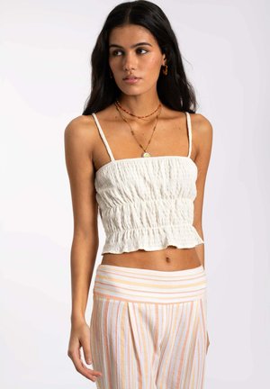 Top de tanque recortado blanco texturizado con tirantes finos y un dobladillo con volantes, combinado con pantalones a rayas en color naranja claro y blanco.