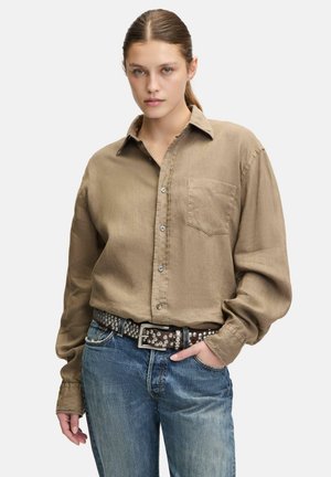 Hemd mit Knopfverschluss aus leichtem braunen Leinen, lange Ärmel, eine Brusttasche. Kombiniert mit blauen Denim-Jeans und einem genoppten braunen Gürtel.