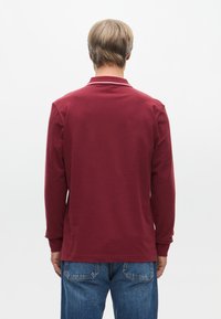 Bordeaux langemouwen polo-shirt met een spread collar, met een minimalistisch ontwerp en ribbenmanchetten. Gecombineerd met blauwe denim jeans.