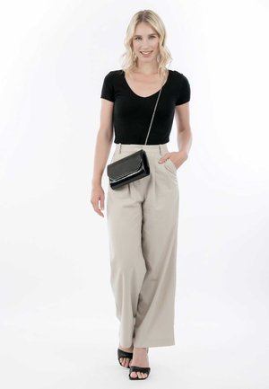 Zwarte getailleerde T-shirt, beige wijde broek en zwarte open teen hakken. Model houdt een kleine zwarte crossbody tas met een kettingstrap vast.