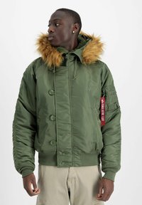 Grüne Bomberjacke mit einem mit Fleece gefütterten Kapuzen, Knopfverschluss, gerippten Bündchen und einer aufgesetzten Tasche am Ärmel mit einem roten Etikett.