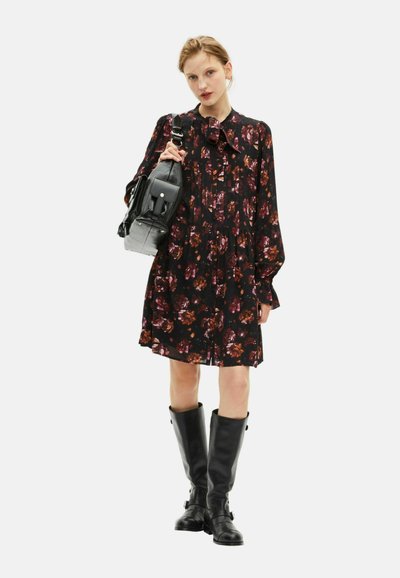 Schwarz mit Blumendessin, mit einer Schleifenkragen, langen Ärmeln und einem gerafften Rock; kombiniert mit einer schwarzen Tasche und knielangen schwarzen Stiefeln.