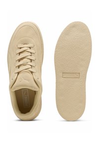 Zapatillas de ante beige con puntera redondeada, cordones planos y suela de goma texturizada. Presenta un logotipo en relieve en la lengüeta y la suela.
