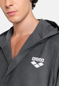 Šedý kapucínkový plášť vyrobený z měkké tkaniny, s žebrovanou texturou podél kapuce a bílým logem "arena" na hrudi.