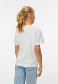 T-shirt en coton blanc avec un col rond classique et des manches courtes, associé à un jean en denim bleu clair, comportant un empiècement au dos et des coutures latérales.