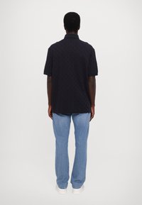 Mørk marineblå polo skjorte med teksturert mønster, korte ermer og klassisk krage. Kombinert med lyseblå straight-leg jeans og hvite joggesko.