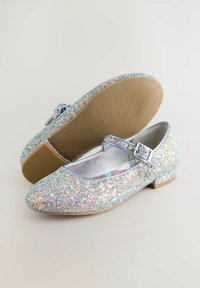 Glitzernde silberne Ballettschuhe mit einer runden Zehe, ausgestattet mit einem Riemen mit einer metallischen Schnalle und einer braunen Gummisohle.