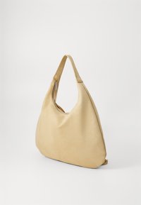Sac hobo en matière beige douce, doté d'une bandoulière unique, d'une forme incurvée et d'une fermeture éclair supérieure pour un accès facile. Texture lisse.