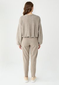 Ensemble en tricot beige composé d'un haut ample avec des manches ballons et un pantalon ajusté, présentant un motif texturé horizontal et une longueur jusqu'à la cheville.