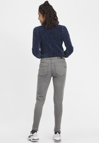 Vaqueros skinny grises con cintura alta, textura ligera, cinco bolsillos y dobladillo deshilachado, combinados con una blusa de manga larga azul marino.