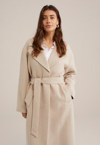 Beige ullblandning kappa med bred krage, bälte i midjan och sidofickor. Mjuk textur och översize silhuett.