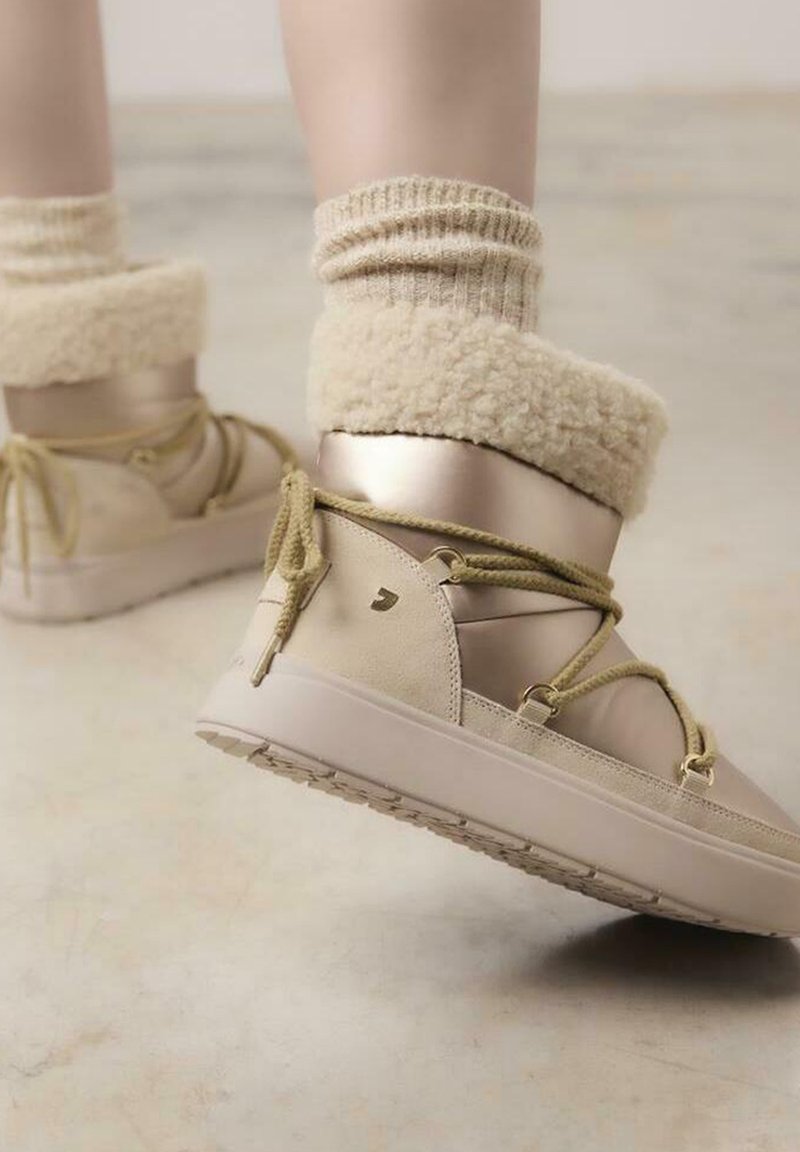 Botas beige con un puño suave y esponjoso, brillo metálico y acentos texturizados. Punta redonda, diseño de cordones y suela de goma con patrón de agarre.