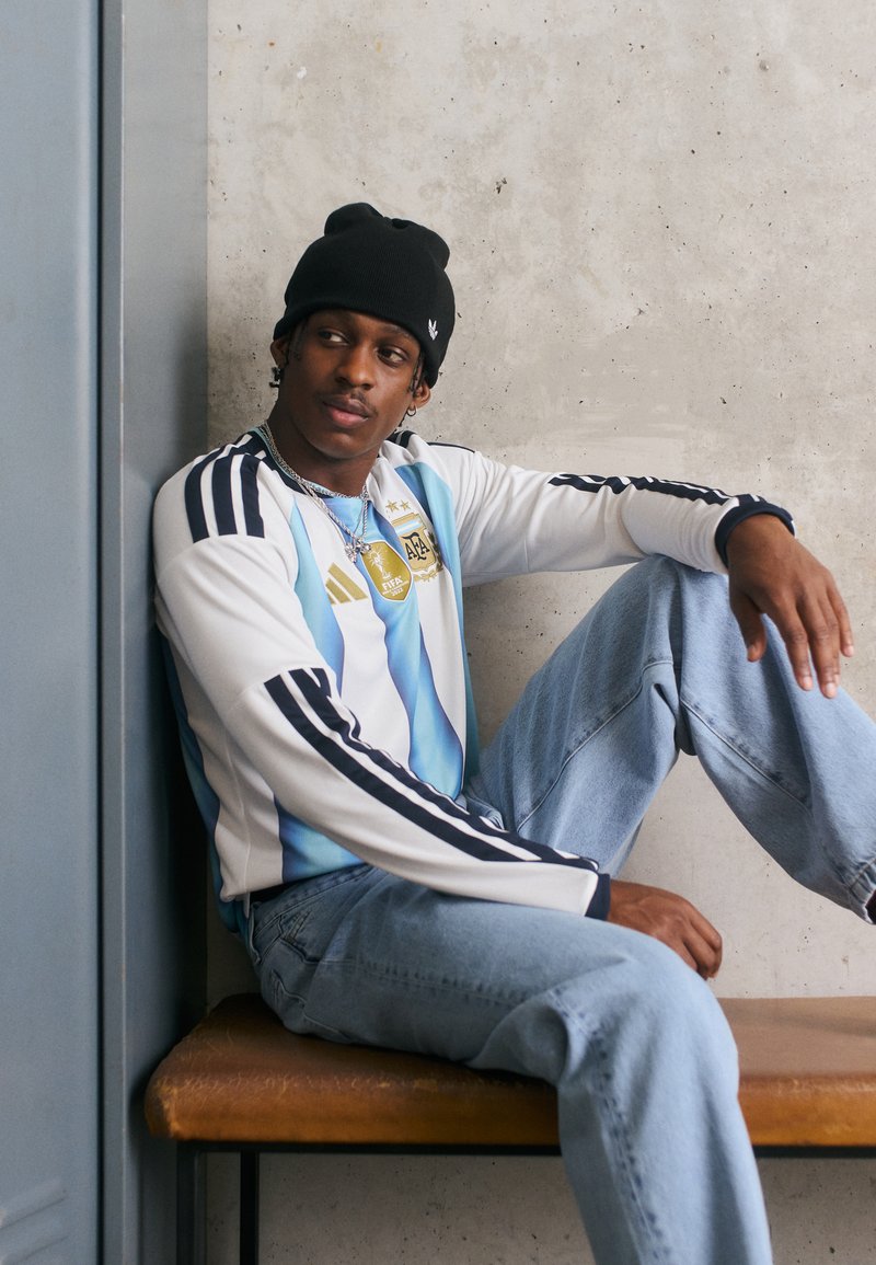 Jersey de manga longa às riscas brancas e azuis claras com detalhes pretos, combinado com jeans azuis claros. Um gorro preto e um colar de corrente completam o visual.