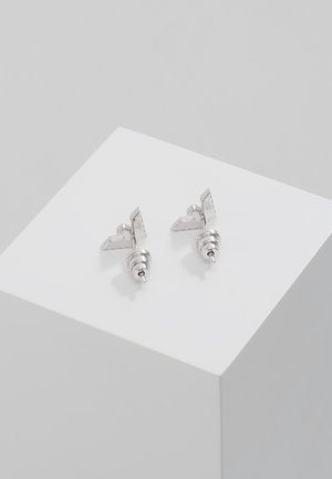 Paire de boucles d'oreilles en argent avec des motifs en forme d'ailes, présentées sur un cube blanc sur un fond neutre.