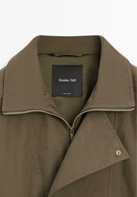 Giacca verde oliva con ampio colletto, cerniera parzialmente aperta, bottone a pressione sul risvolto e etichetta nera Massimo Dutti all'interno del colletto.