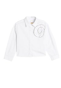 Camisa blanca de manga larga con cuello y adorno de flor de tela en el lado izquierdo del pecho. Hecha de algodón con una textura suave.