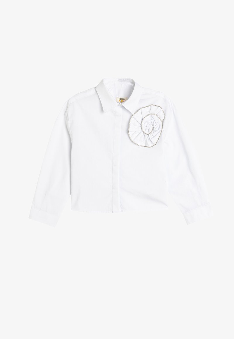 Witte langemouwen shirt met een kraag en stoffen bloemversiering op de linkerborst. Gemaakt van katoen met een gladde textuur.