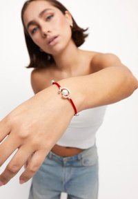 Pulsera de goma roja con un acento circular plateado y una perla, con cuentas plateadas a cada lado. Diseño simple y moderno.