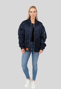 Marine bomberjack featuring een gequilte design, ritssluiting, geribde manchetten en een oranje label aan de zoom. Draagt over een zwart top.