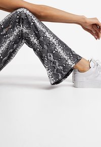 Pantaloni a gamba larga con stampa serpente in bianco e nero, dal tessuto liscio, abbinati a sneakers bianche con plateau.