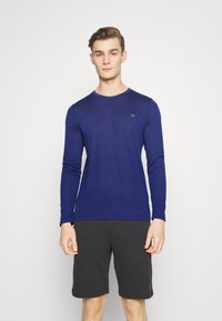 Long-sleeve navy blue t-shirt made of smooth fabric, featuring a crew neckline and a small logo on the chest, paired with black shorts.