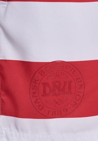 Rot-weiß gestreifter Stoff mit einem strukturierten, kreisförmigen Logo, das "DBU" in der Mitte zeigt. Glatte Textur, Design eines Sportshirts.