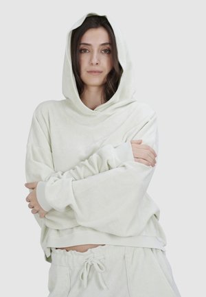 Helle grüne Kapuzenjacke aus weichem, strukturiertem Stoff mit weitem Ärmeln und gerippten Bündchen; getragen mit passenden Jogginghosen.
