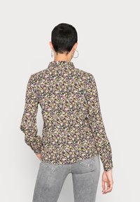 Blouse florale avec un fond noir, ornée de petites fleurs roses, jaunes et blanches. Manches longues et col. Tissu léger.