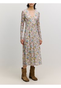 Blumen langärmliges Kleid mit V-Ausschnitt, in zarten Farben und mit tailliertem Oberteil. Getragen mit braunen Stiefeletten. Glatte Stoffstruktur.
