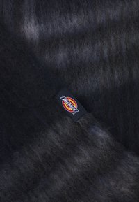 Sort og grå gradientstof med en blød, fuzzy tekstur, der har et Dickies-logo patch i livlig rød og gul på en sort baggrund.