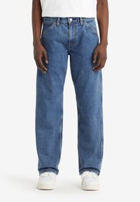 Blå denimjeans med raka ben, femfickor och subtila sömnadsdetaljer, i kombination med vita sneakers.