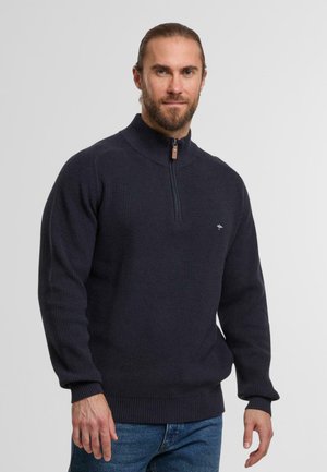 Marineblauer, gerippter Strickpullover mit einem halbseitigen Reißverschlusskragen und braunem Reißverschluss. Verfügt über ein kleines Logo auf der Brust und hat eine lockere Passform.