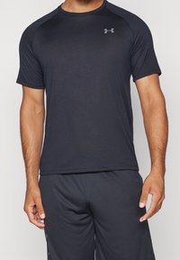 Svart atletisk t-shirt med korta ärmar, tillverkad av slät, flexibel tyg. Har en subtil logotyp i grått på vänster bröst.