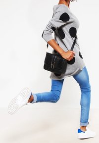 Šedý tunikový top s černými puntíky, se zipovými detaily, doplněný modrými džínami, bílými teniskami a černou kabelkou přes rameno s texturovaným povrchem.