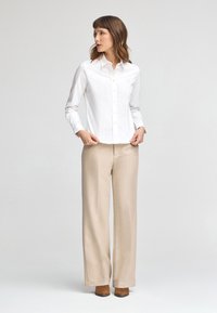 Camisa blanca de botones con cuello y mangas largas, combinada con pantalones de pierna ancha beige y botas de tacón marrones hasta el tobillo.
