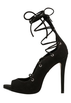 Musta suede korkokenkä avokannan ja ympäri nilkan kiinnitettävillä naruilla.