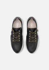 Sneakers in pelle nera con lacci accentati in oro e cerniera. Presentano una suola bianca imbottita e una superficie liscia e lucida.