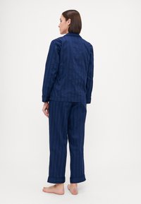 Mørkeblå pyjamassett med en jevn tekstur. Toppen har krage, lange ermer, og er kombinert med matchende tapered bukser.