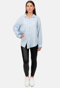 Lichtblauw overhemd met witte stippen, lange mouwen en een comfortabele pasvorm, gecombineerd met zwarte leggings en witte sneakers.