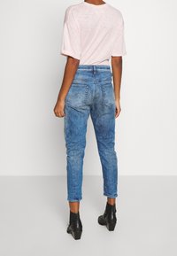 Tajta jeans i blekt blå denim med hög midja, med bakfickor och en avsmalnande bendesign. Bärs med en ljusrosa t-shirt.